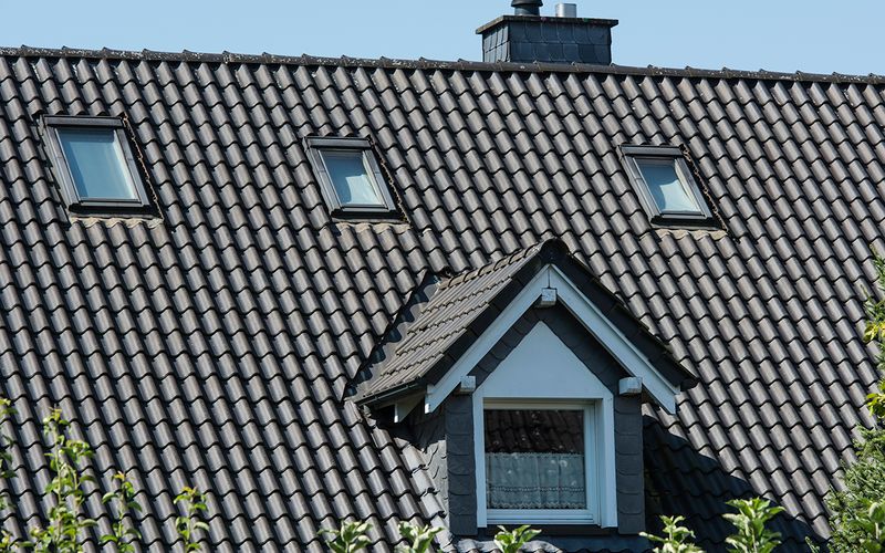 Ein gepflegtes Hausdach mit dunklen Ziegeln, weißen Dachfenstern und einem kleinen Giebel.