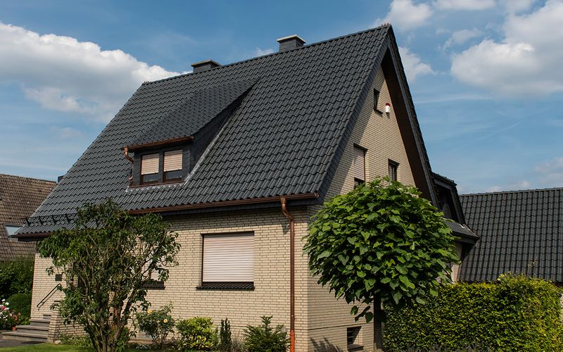 Ein zweistöckiges Einfamilienhaus mit hellem Ziegel, dunklem Dach und gepflegtem Garten in ruhiger Wohngegend.