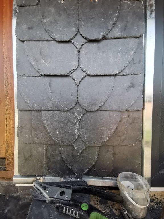 Schieferplatten in Fischschuppenmuster, umgeben von Werkzeugen, deuten auf handwerkliche Arbeiten hin.