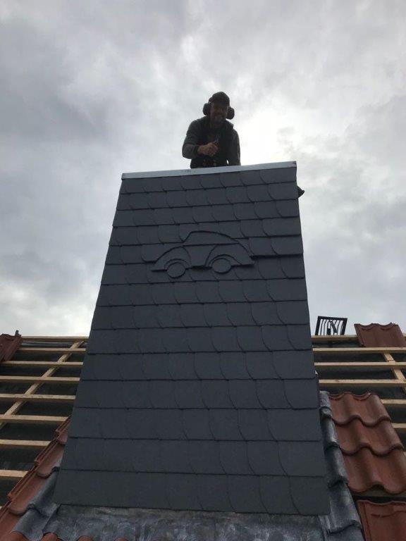 Ein Mann arbeitet auf einem Dach mit einem Schornstein, der mit Auto-Design-Schindeln verkleidet ist.