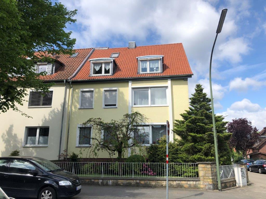 Ein gelbes Wohnhaus mit Garten, Baum und geparktem Auto an einem sonnigen Tag in einer ruhigen Straße.