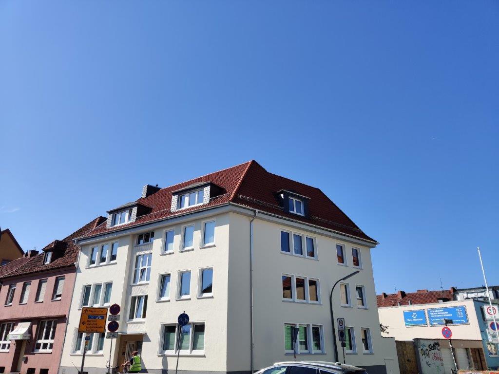 Straßenszene mit mehrstöckigen Wohngebäuden, roten Ziegeldächern und Verkehrsschildern bei sonnigem Wetter.